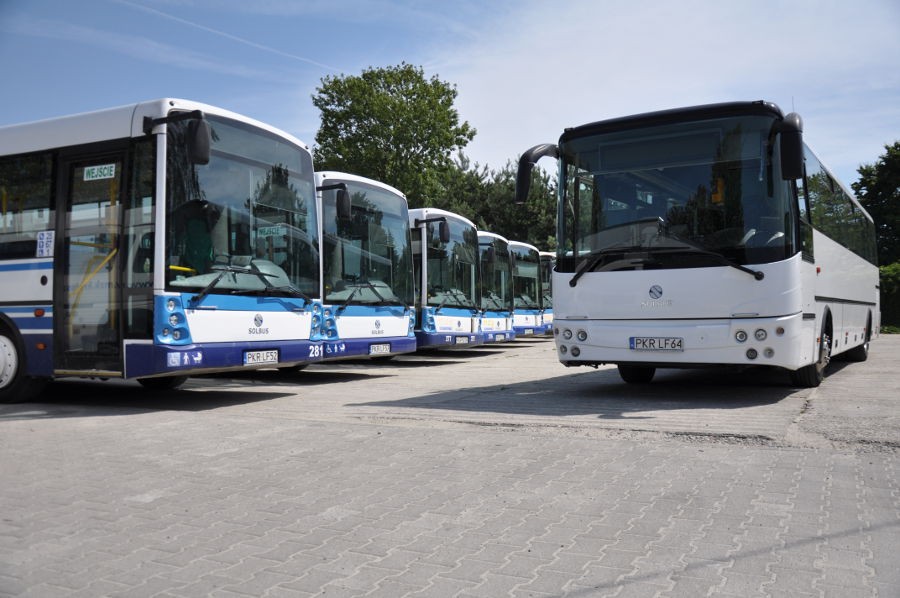 Prezentacja biało-niebieskich autobusów Solaris, sześć autobusów stojących obok siebie. Na pierwszym planie widoczny biały autokar Solbus.