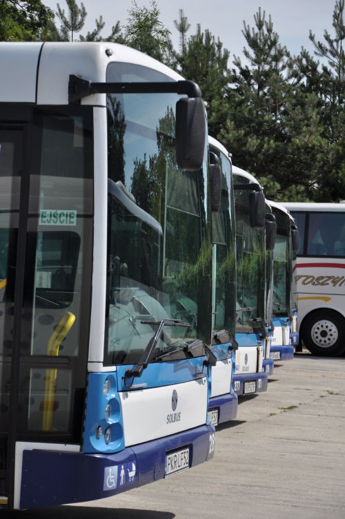 Prezentacja biało-niebieskich autobusów Solaris, cztery autobusy stojących obok siebie. W tle biały autokar z żółtym napisem.