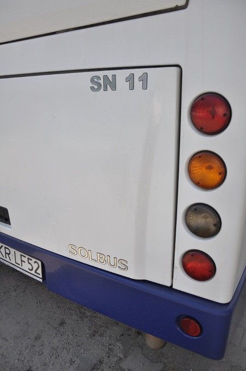 Prezentacja białego autokaru Solbus, widoczny tył pojazdu i światła drogowe.